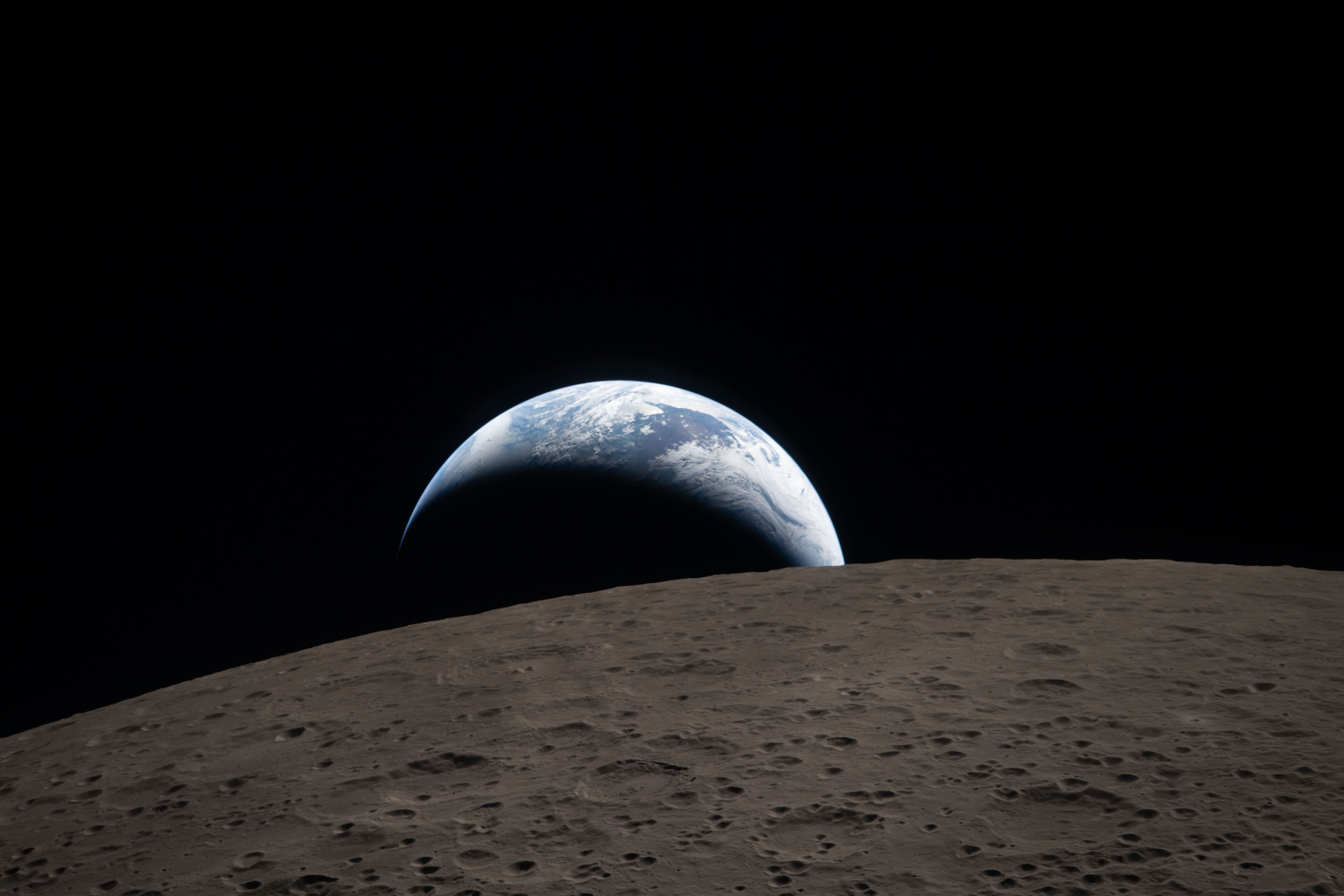Earthset（art002e009288）。月面の前景にはオーム・クレーターの段丘とセントラルピークが見える。地球は三日月状で、昼側のオーストラリア・オセアニア上空の雲だけが白く光る。