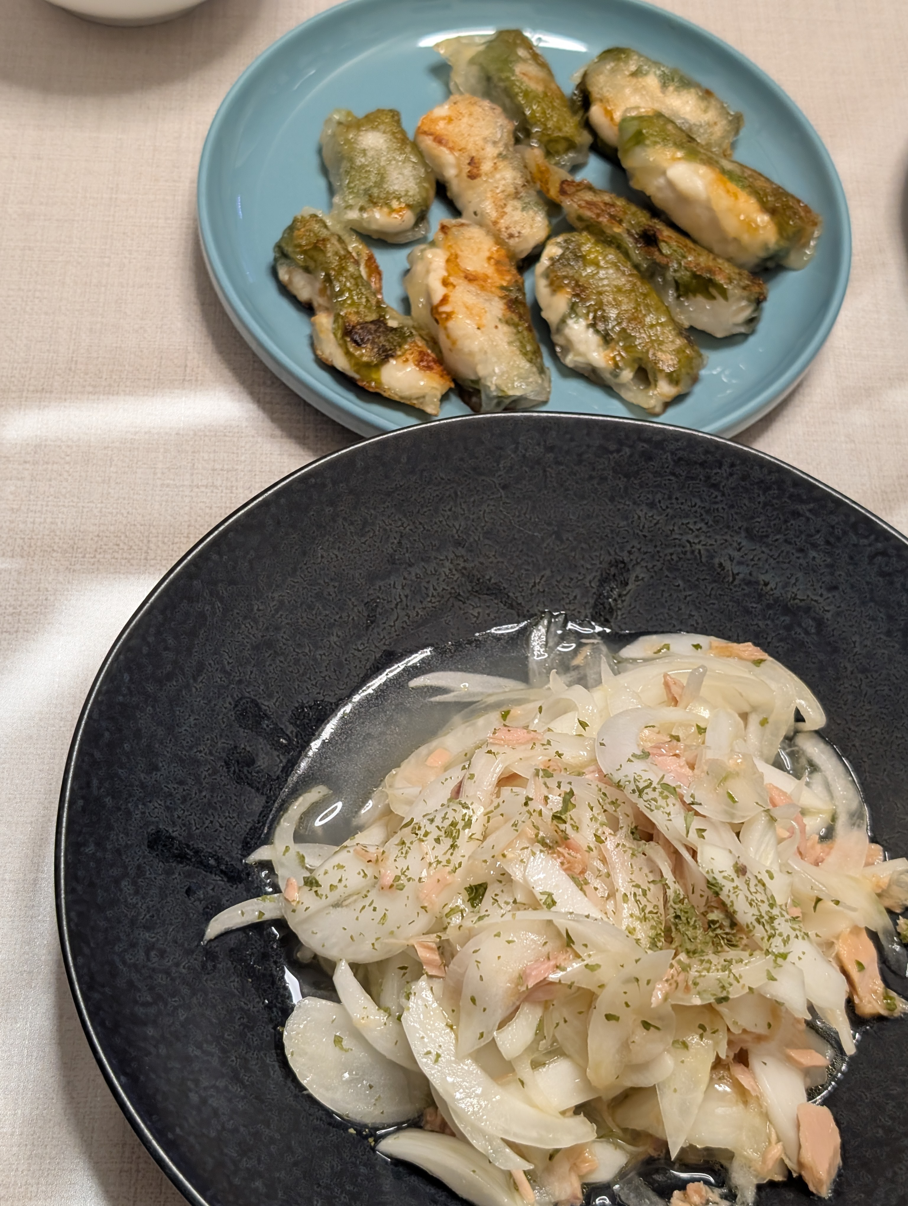 黒い器のオニオンツナサラダと青い皿の鶏肉の磯辺焼き