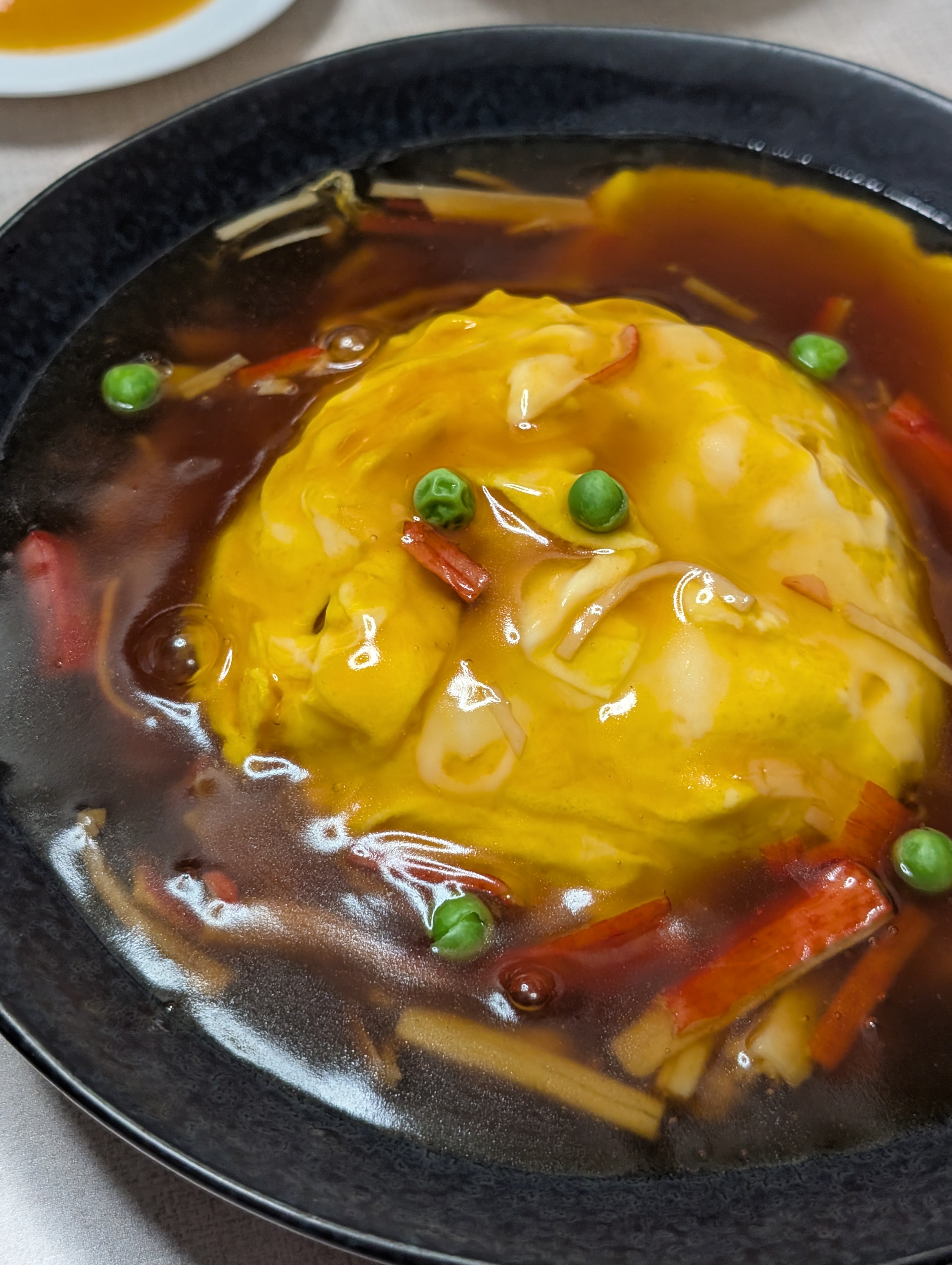 黒い器に盛られた天津飯。甘めのあんにたけのこ、カニカマ、グリーンピースが入っている