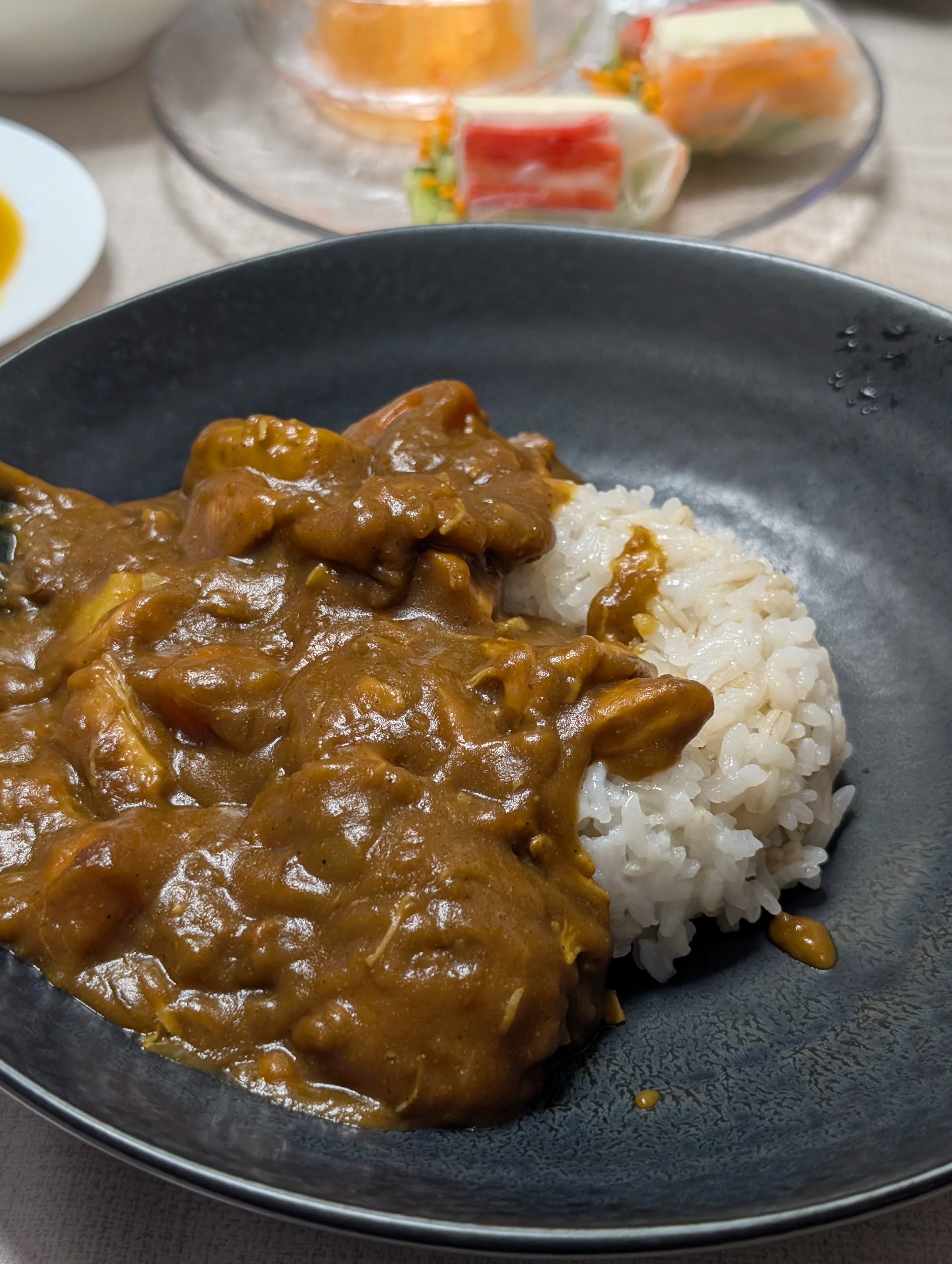 黒い皿に盛られた妻特製のカレーライス。奥にカニカマ入りの生春巻きが添えられている