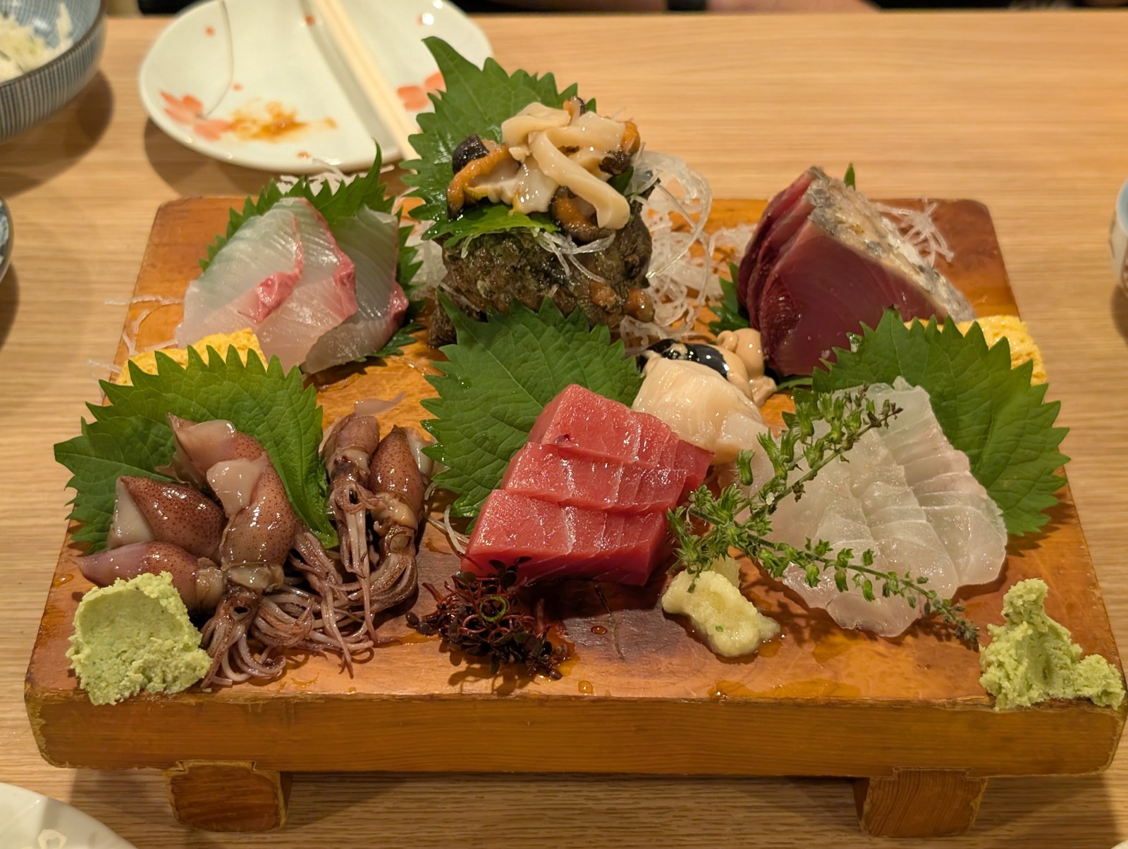 木の板に盛られた刺身の盛り合わせ。ほたるいか、赤身、カツオ、白身、殻に盛ったあわび