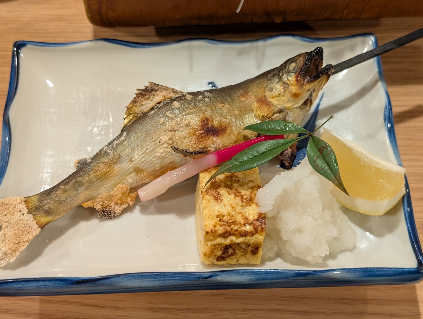 串を打った鮎の塩焼き。出汁巻き卵、大根おろし、はじかみ、レモンが添えられている