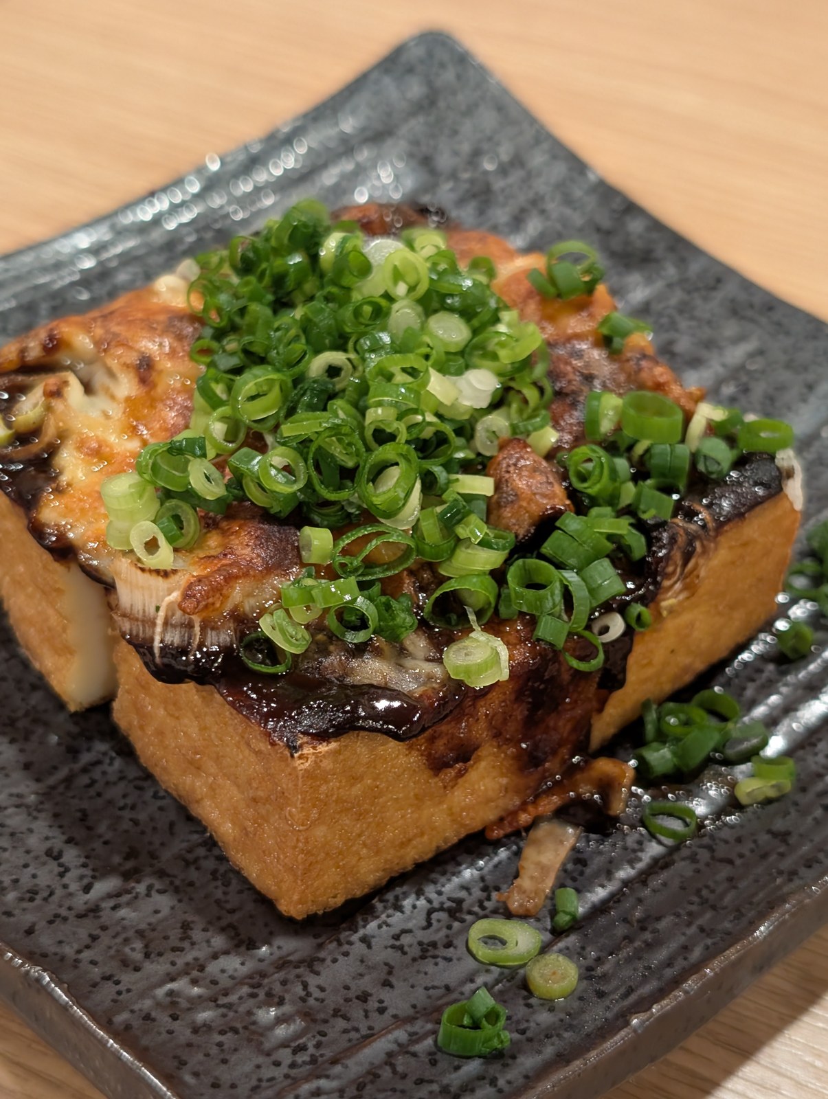 黒い皿にのった厚揚げの味噌チーズ焼き。刻んだ九条ねぎが山盛りにかかっている