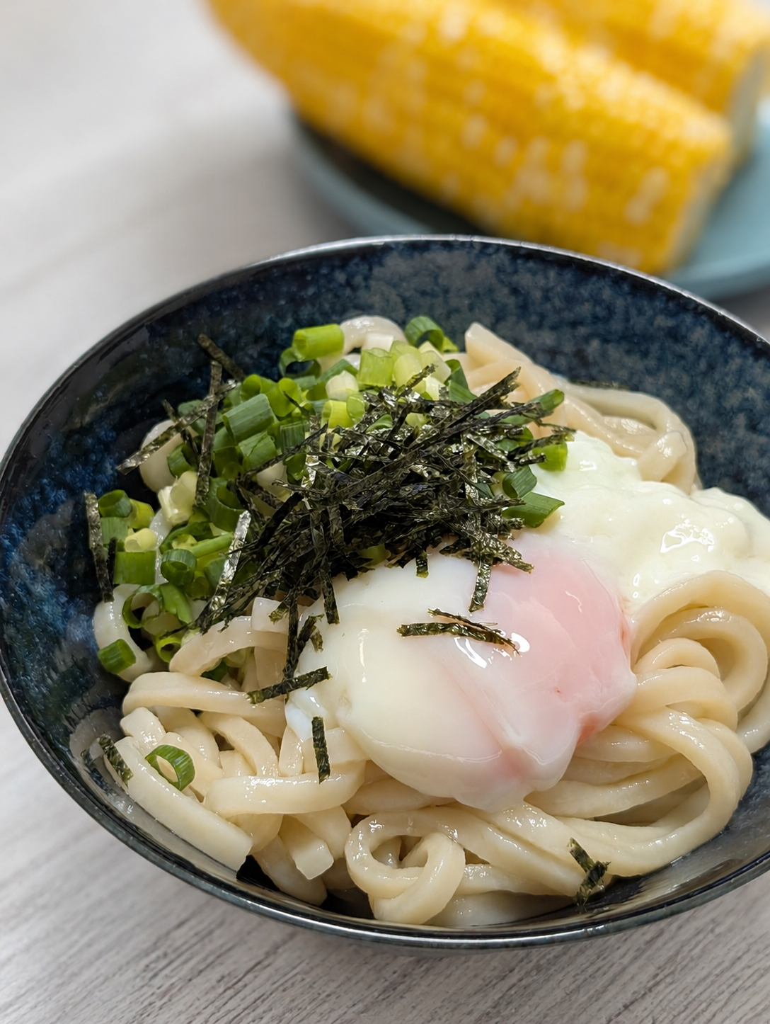 温泉卵とねぎと刻み海苔を乗せたぶっかけうどん、奥にとうもろこし