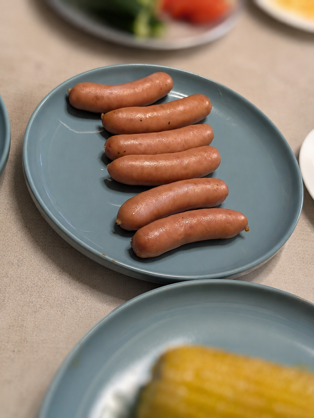 青い皿に並んだウインナー6本。奥にきゅうりとトマト、手前に焼きとうもろこし