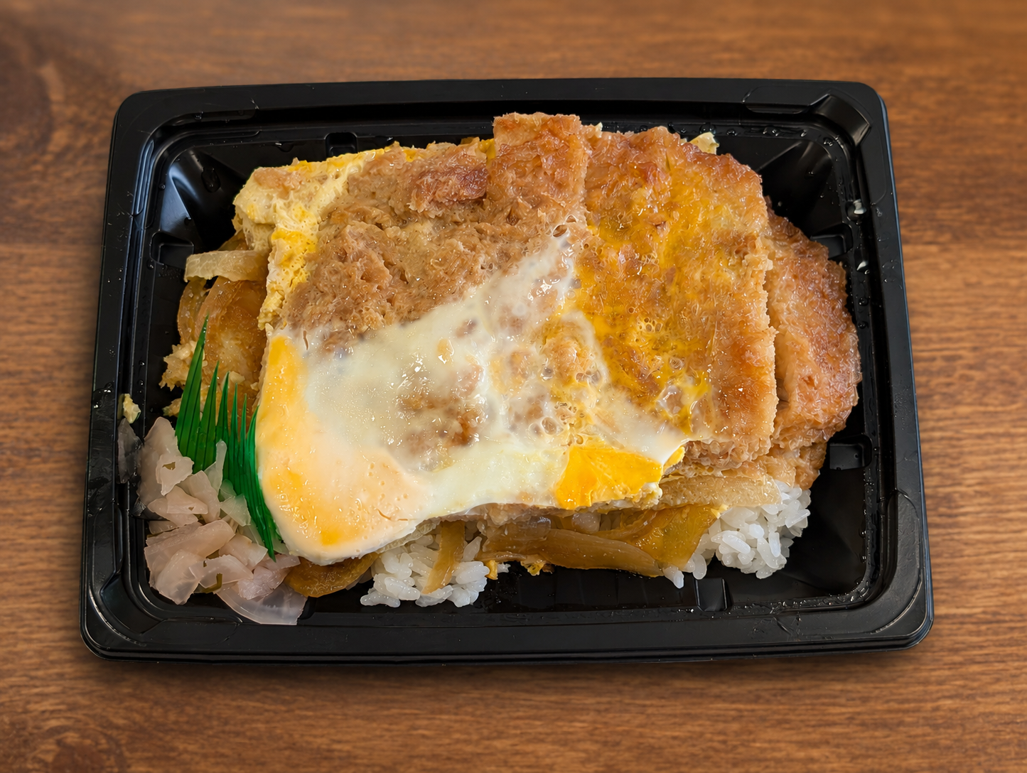 黒い容器に入ったテイクアウトのカツ丼。卵とじのカツとごはん、隅に紅生姜