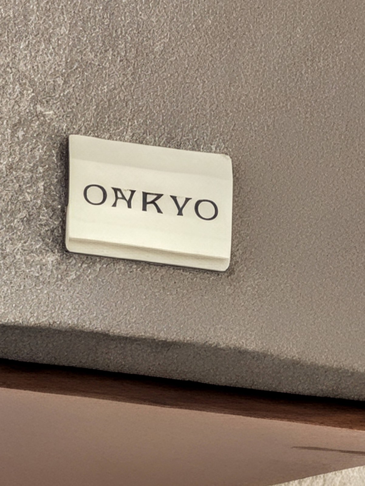 スピーカーのグレーの布地に付いたONKYOのロゴプレート。Nの字が逆Vのような形に崩れている