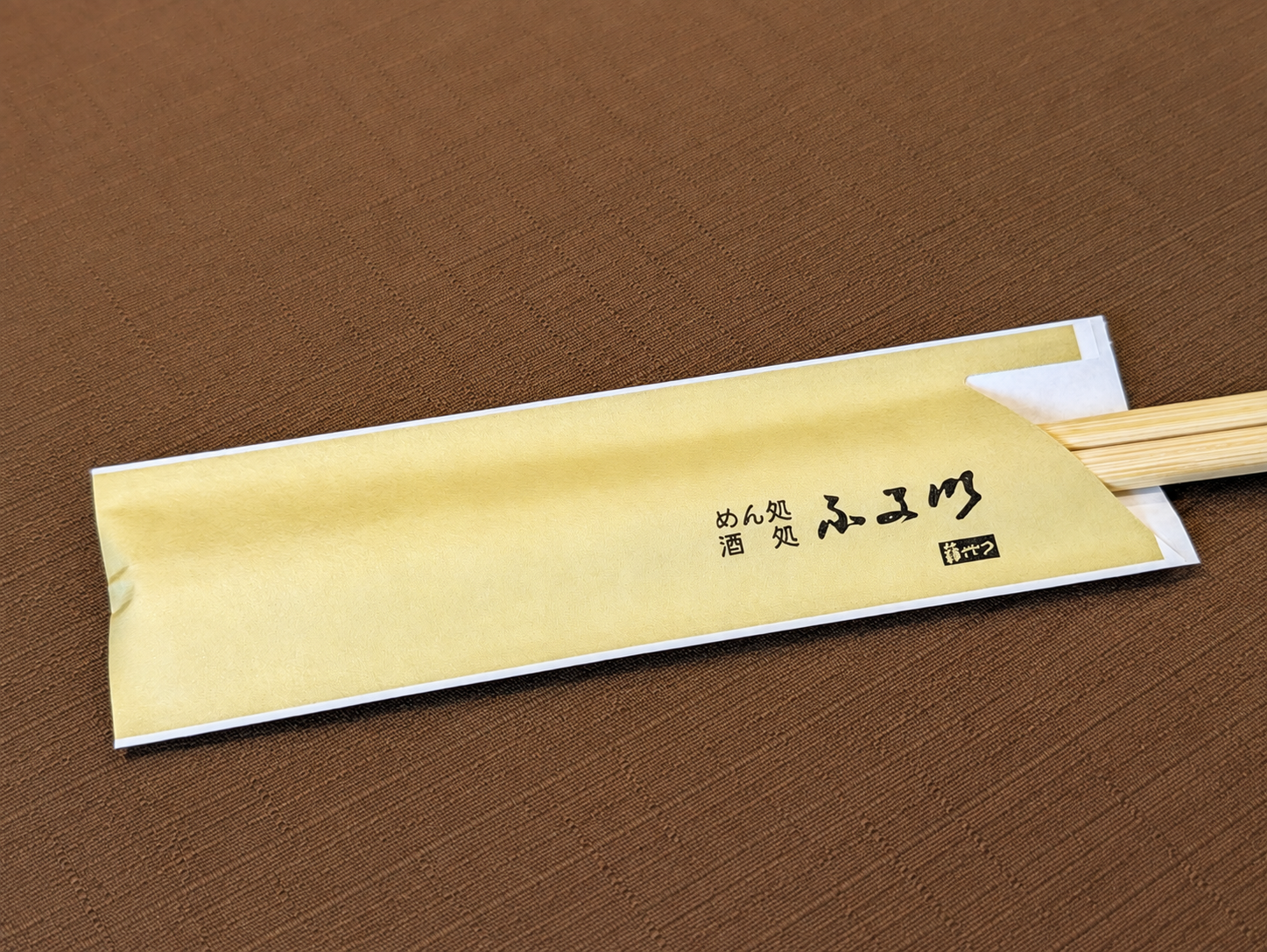 茶色いテーブルに置かれた、めん処 酒処 ふる川 暮六つと書かれた黄色い箸袋