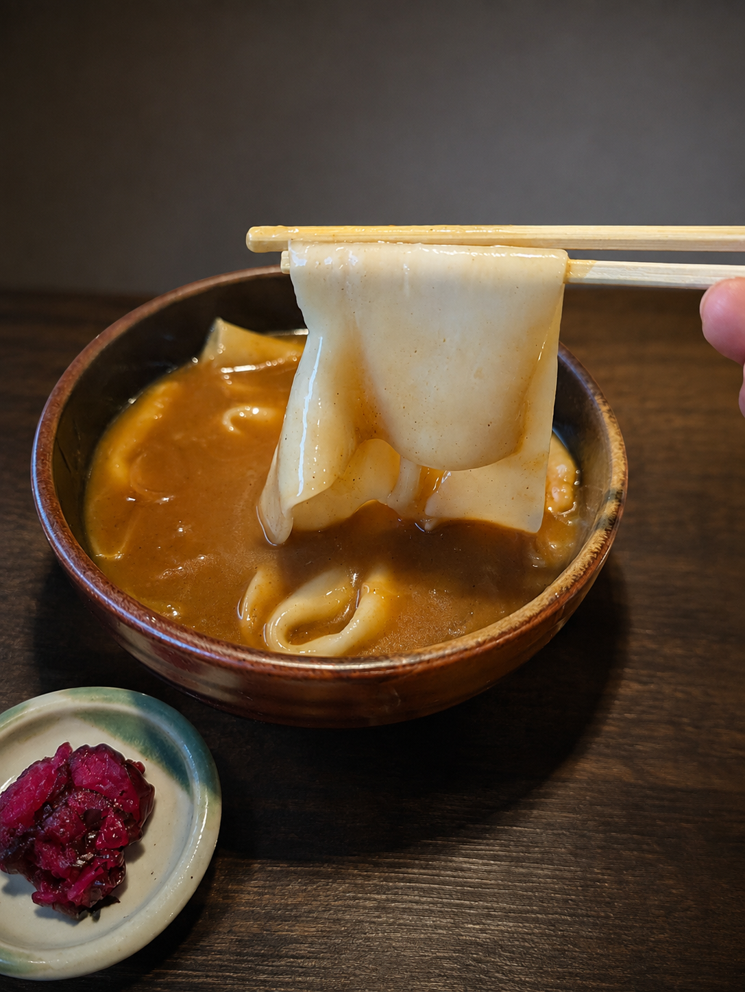 箸で持ち上げた幅の広いひもかわうどん。カレーがしたたっている