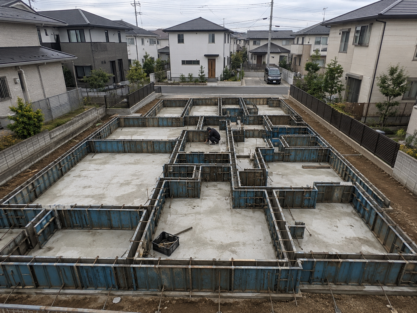 ベタ基礎に青い型枠パネルが立ち、中で作業員がひとり作業する新築工事の現場