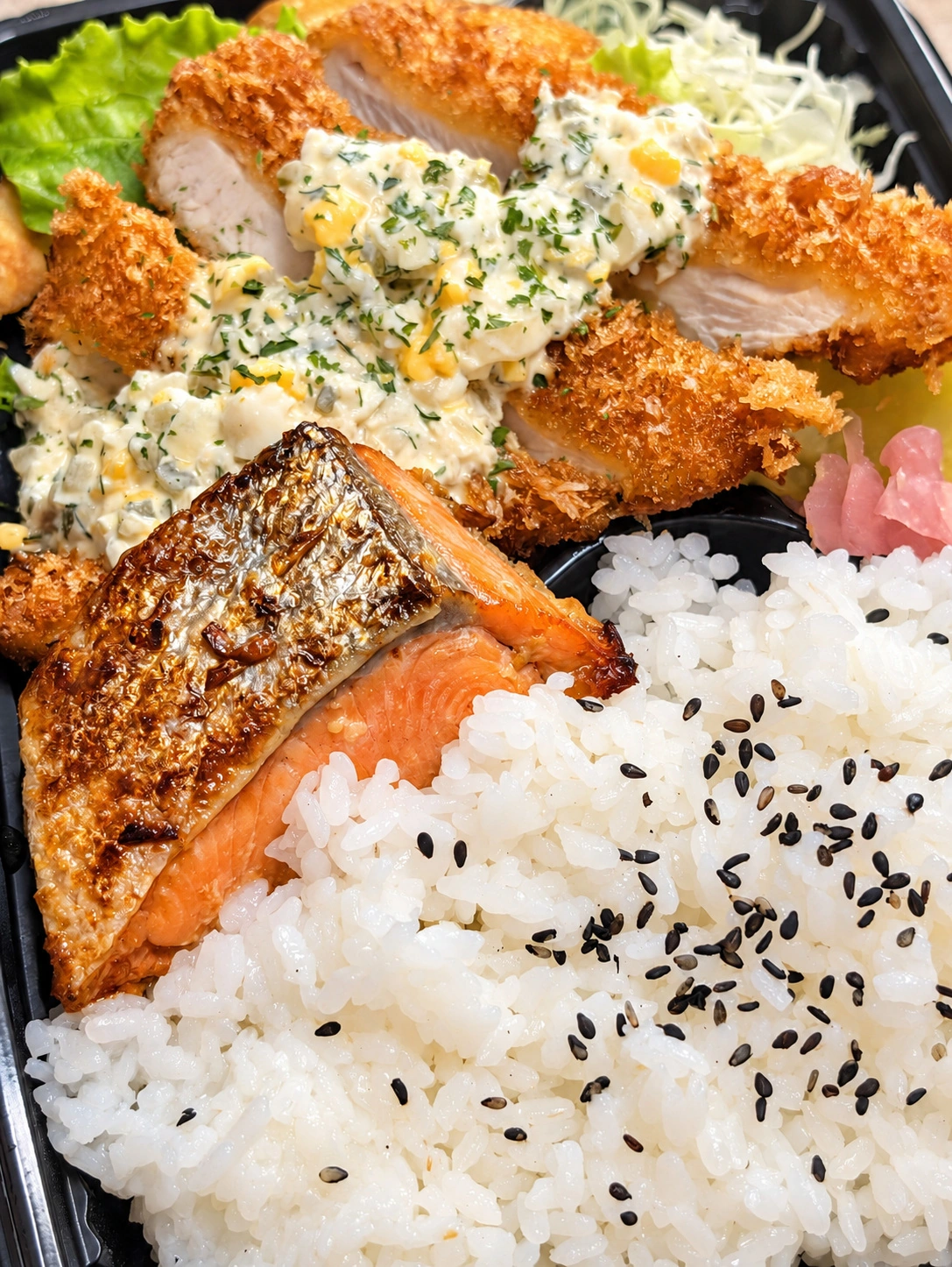 焼き鮭とタルタルソースのかかった揚げ物、ご飯が入った弁当（AIで光と色味を調整）