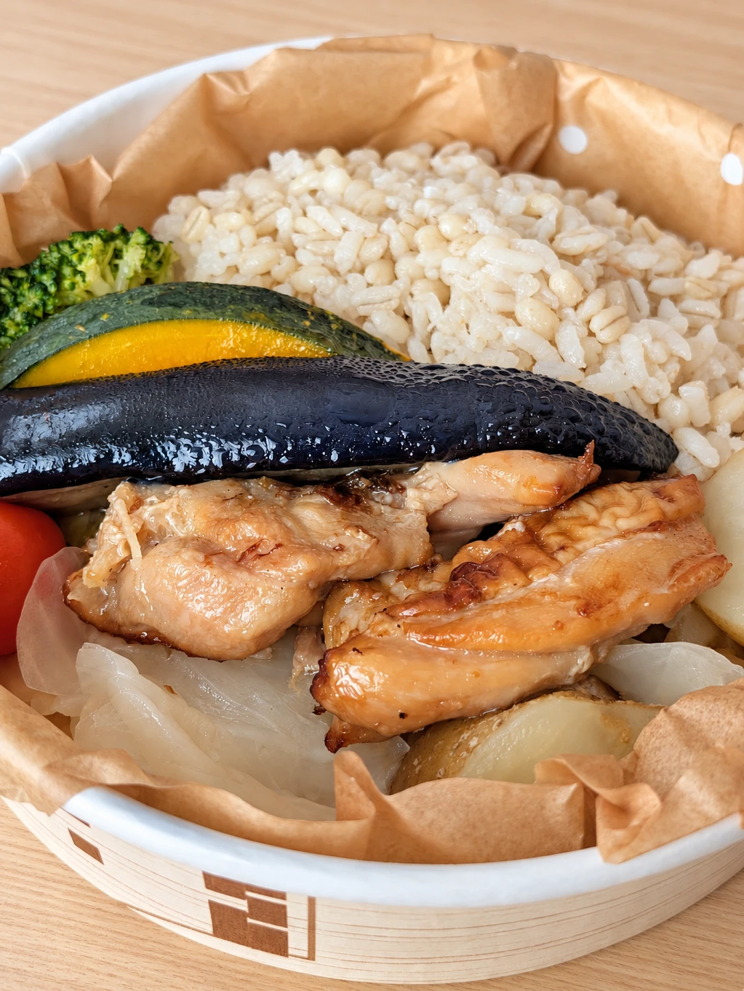 ご飯と肉、かぼちゃ、なすなどが入った丸いお弁当（卓上と明るさはAIで加工）