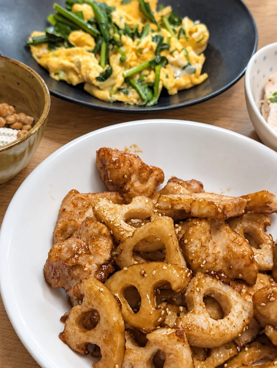 れんこんと鶏肉の炒め物、ニラ玉、納豆、冷ややっこが並ぶ夕食(卓上と明るさはAIで加工)