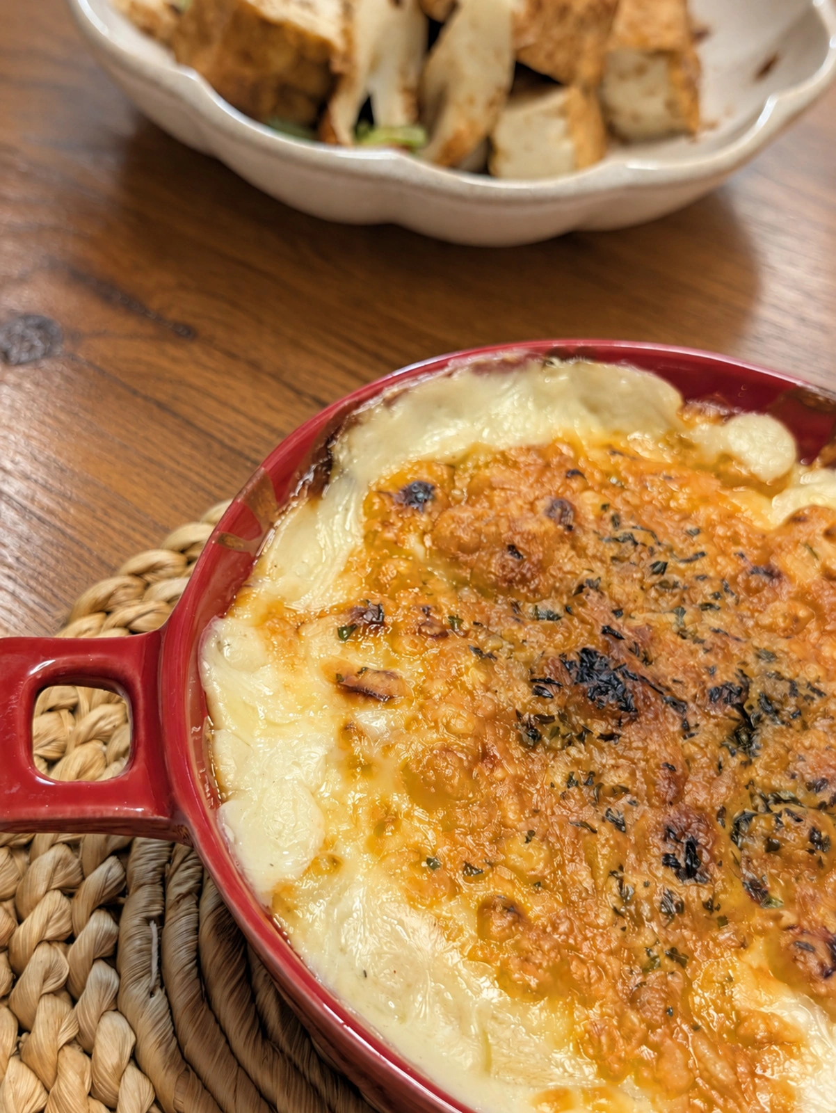 夕食のドリア。赤い耐熱皿と奥の小鉢(卓上はAIで加工)