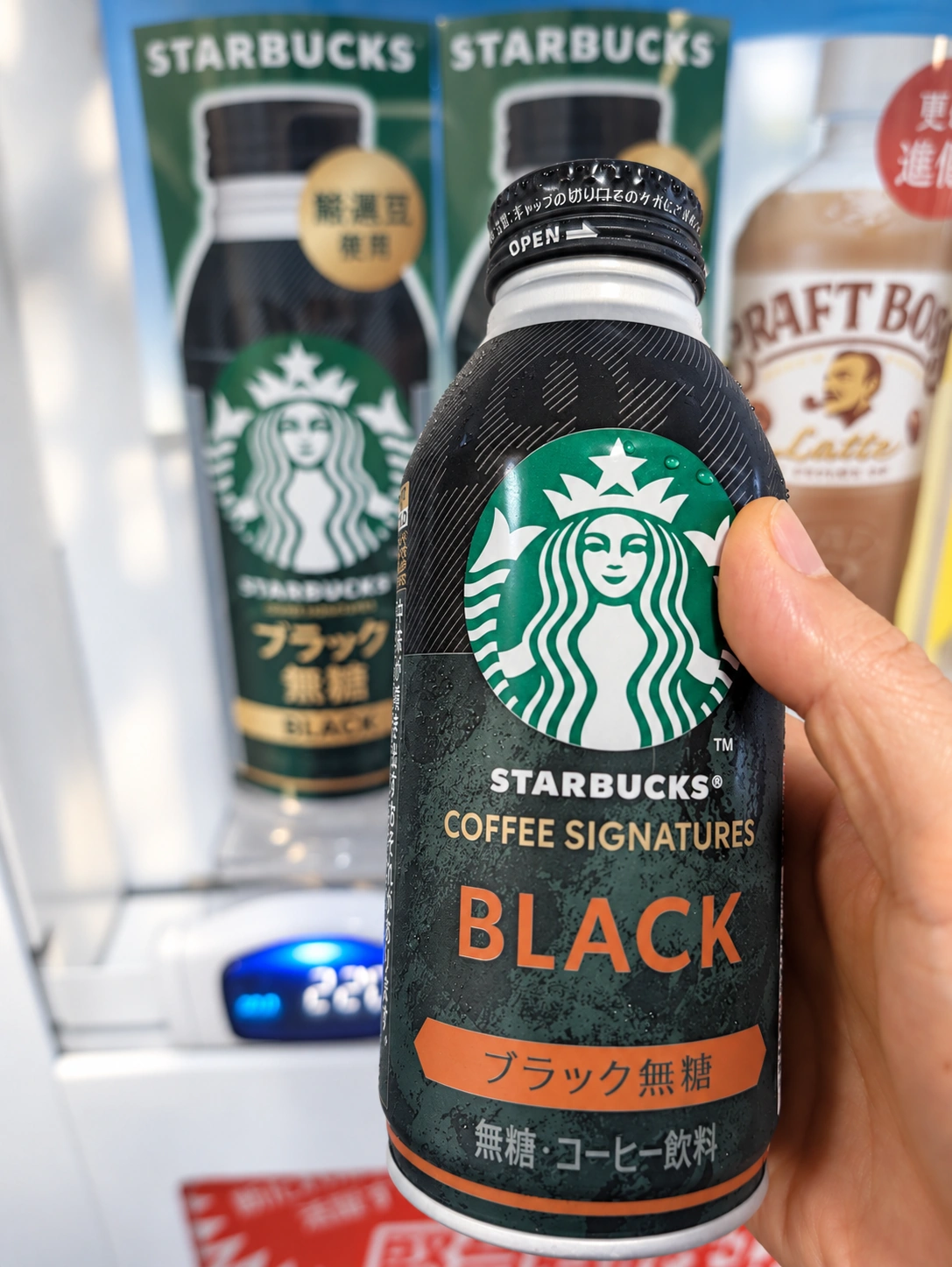 自販機の前で手に持ったスターバックス コーヒーシグネチャー ブラック無糖のボトル缶(背景はAIで加工)
