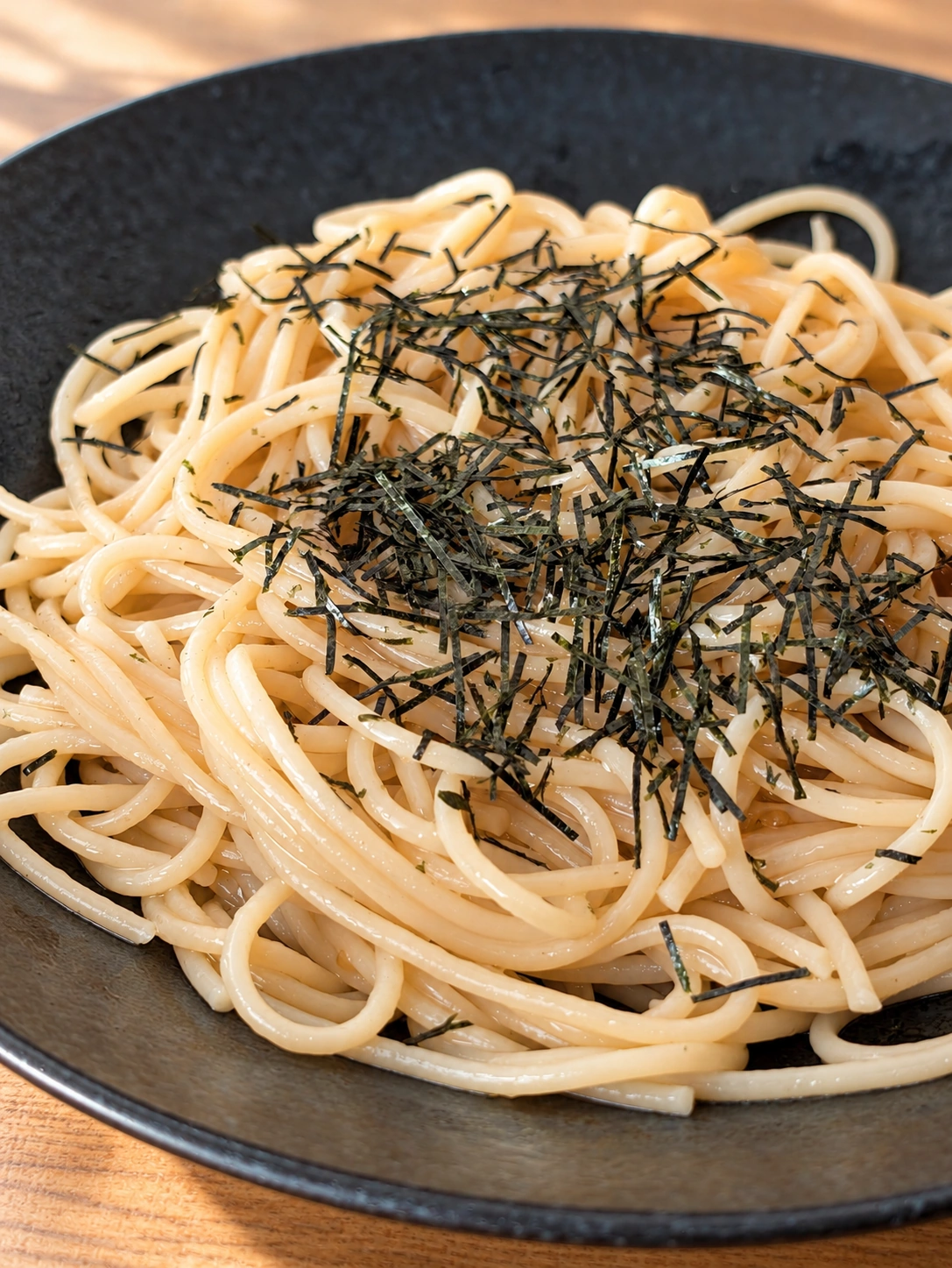 黒い皿に盛った海苔のせ明太パスタ（卓上などはAIで加工）